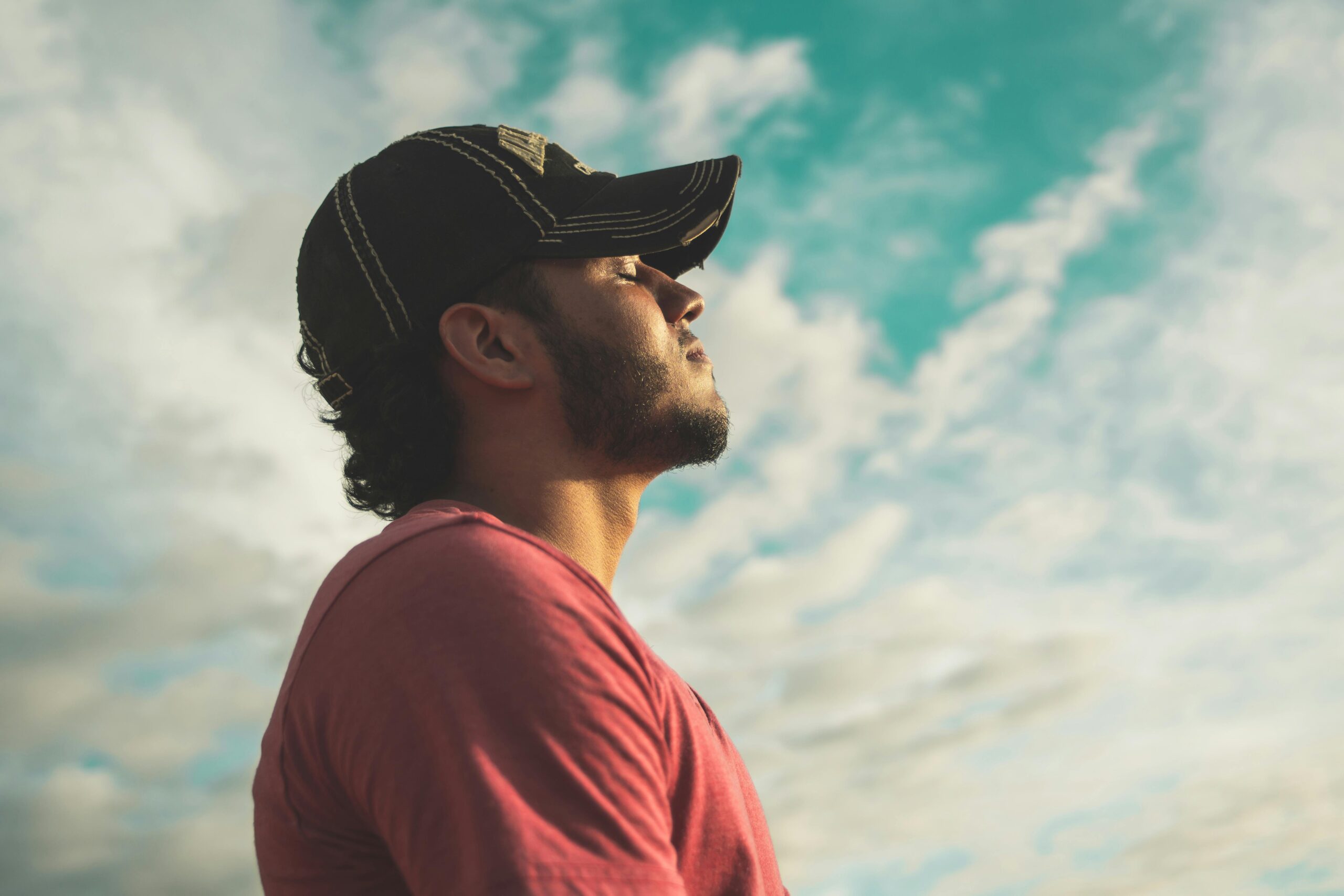 young man in baseball cap has eyes closed as he takes a big breath of fresh air