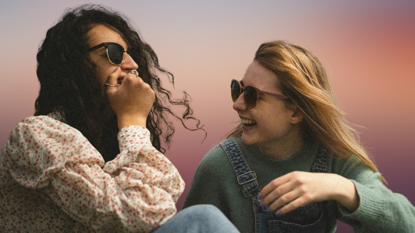 Foto de duas jovens rindo juntas ao ar livre sob o sol. Ambas usam óculos de sol. Imagem fornecida por BABI no Unsplash.